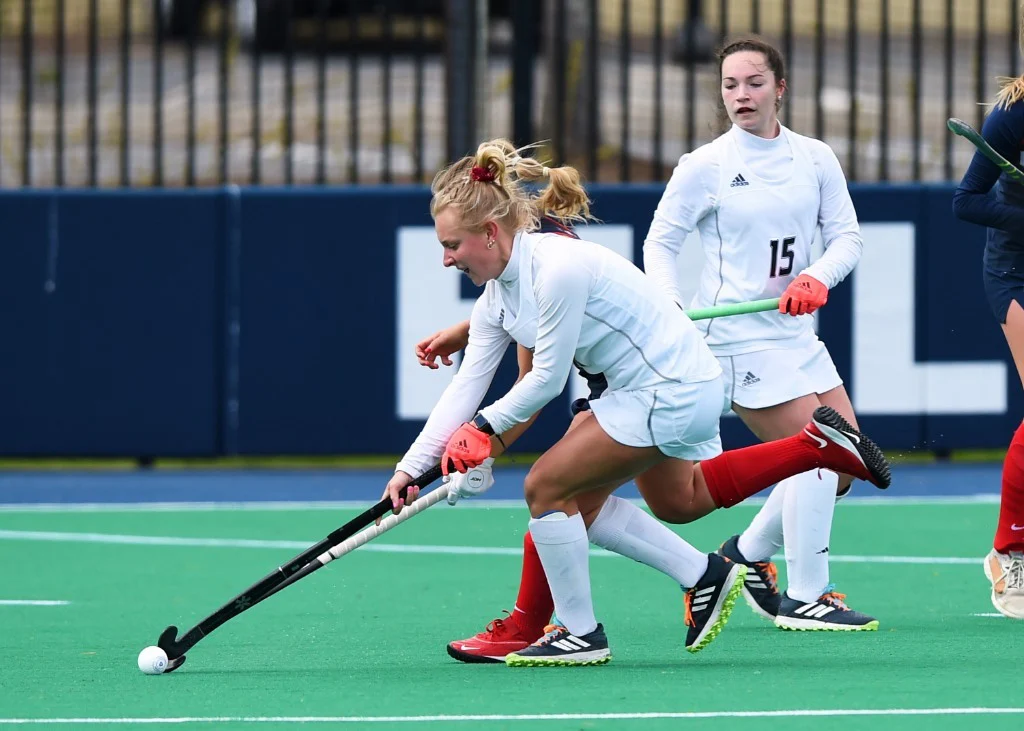 Group of young women chasing a ball on field hockey field.